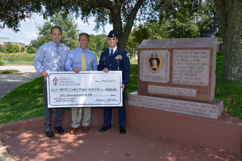 Michles & Booth attorneys Marcus Michles (center) and Chris Janes (left) present the 2nd Annual Marcus R. Michles ROTC Scholarship to Cadet Major Jack Fite in front of the Purple Heart Memorial in Pensacola, which – like the scholarship – also honors Michles’ father.